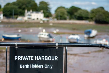 Photo for Private harbour berth holders only black sign at a pretty harbor at low tide. Softly focused boats sitting on the mud in the background contrast the sharply focused black warning sign and railings - Royalty Free Image