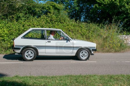 Photo for Powderham, Devon, uk. July 9th 2022. Ford Fiesta XR2 classic car in white driving along a country road. Fast ford with alloy wheels, collective and desirable historic vehicle. - Royalty Free Image