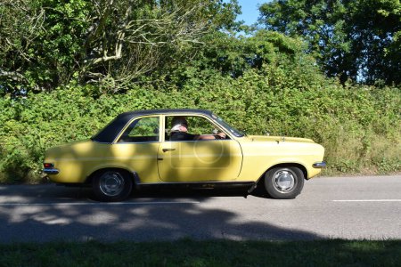 Photo for Powderham, Devon, UK. July 9th 2022. Vauxhall Viva HC classic car in yellow. Two door saloon car with a black vinyl roof driving on a summers afternoon. - Royalty Free Image