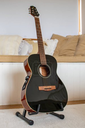 Photo for Banwell, North Somerset, uk. March 8th 2022. Voyage Air foldable travel acoustic guitar sits on a stand. Unique hinged guitar fols in half. Black electro acoustic guitar. Portable traveling guitar - Royalty Free Image