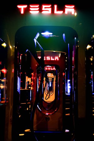 Foto de Exeter, Devon, Reino Unido. 11-11-23. Una línea de estaciones de carga Tesla fotografiadas por la noche. Una imagen única con un tema muy oscuro y colorido. Carga de vehículos eléctricos. EV. - Imagen libre de derechos
