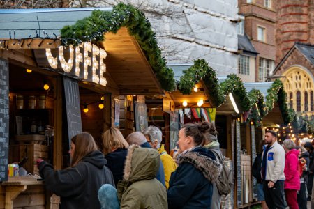 Téléchargez les photos : Exeter, Royaume-Uni. 11-28-23. Marché de Noël Exeter avec des acheteurs achetant du café chaud auprès d'un vendeur de café festivement décoré. Les gens faisant la queue dans des vêtements d'hiver avec un thème de Noël fort tout au long. - en image libre de droit