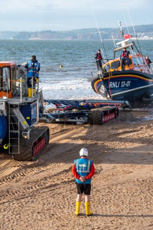 Photo for Exmouth, Devon, uk. 02-15-24. RNLI Lifeboat crew prepares to retrieve a Shannon class lifeboat at Exmouth lifeboat station. Copy space. Selective focus on the man standing on the beach. - Royalty Free Image