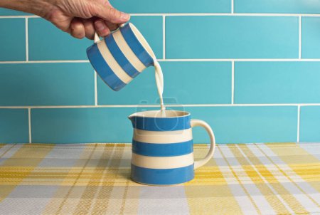 Image de lait avec une cruche bleue et blanche versant du lait frais dans une autre cruche similaire. Couleurs bleu blanc et jaune. Concept de produits laitiers.