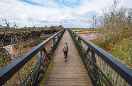 Cycling image of a lady on a bicycle riding across a bridge. Wide angle image with good symmetry. Selective focus on the cyclist. Concept image of  a healthy lifestyle and exercise. 