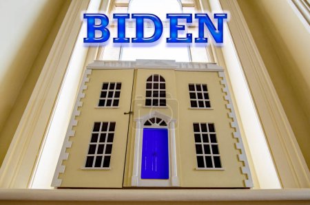 BIDEN. Politisches Konzeptbild mit dem Wort BIDEN in blau über einem Musterhaus mit blauer Tür. Bild Präsidentschaftswahl 2024. Selektive Fokussierung auf die Oberseite der Tür. 