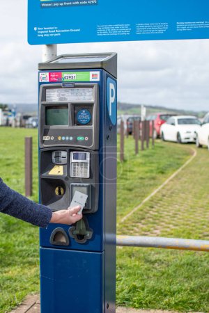 Photo for Exmouth, Devon, uk. 03-20-24. Car park payment machine with a woman inserting a debit card into the machine to pay for parking. - Royalty Free Image