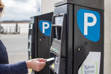 Máquina de pago del aparcamiento con una mujer que presenta una tarjeta de débito a la máquina para pagar el estacionamiento. 