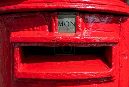 Palabra del lunes mostrada como MON en un buzón rojo británico. Imagen en formato retrato visualmente llamativa y colorida que representa el día de la semana. Rojo brillante. Buzón e imagen postal. 
