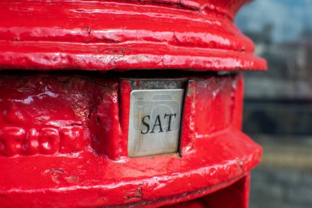 Saturday word shown as SAT on a British red letter box. Visually striking and colorful portrait format image depicting the day of the week. Bright red. Letter box and postal image. 