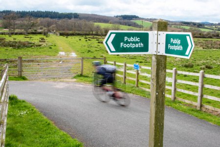 Panneau du sentier public. Un cycliste en mouvement flou parcourt une piste cyclable. Concentrez-vous sélectivement sur le panneau. Contexte de la campagne.