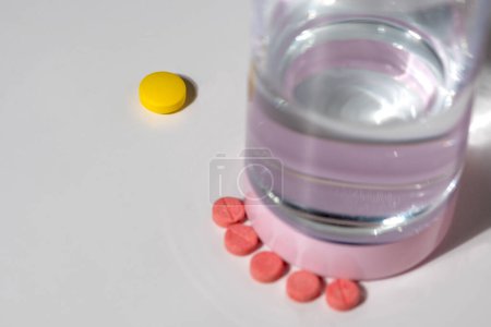 Foto de Píldoras de colores y un vaso de agua sobre un fondo blanco - Imagen libre de derechos