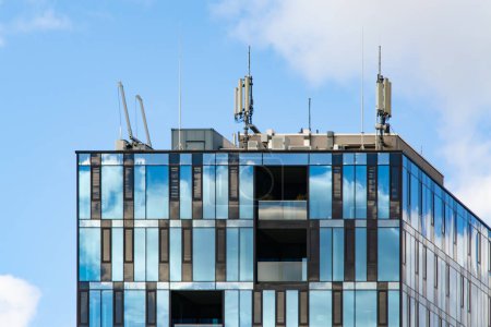 Photo for Mobile cellular communication antennas on the roof of a modern building. Clouds are reflected in the reflective surface of the building. - Royalty Free Image