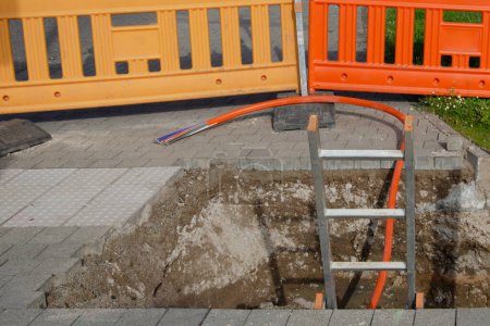Photo for Fibre optic cable installation and ladder in the excavation. Orange fence in background. - Royalty Free Image