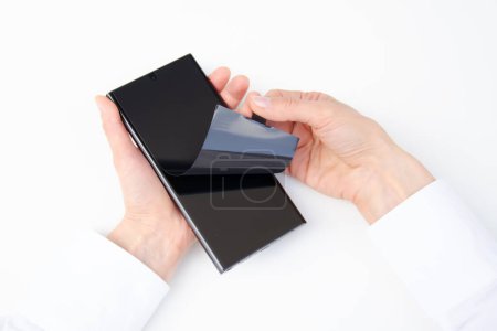Photo for Unpack new smartphone. Removing protective black film from a new phone. Close-up of a woman's hands . White background. Smartphone samsung galaxy S23 ultra. - Royalty Free Image