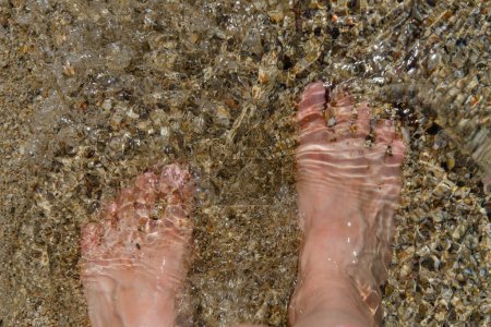 Photo for Barefoot women's feet close-up in clear water on the sandy bottom. The glare of the sun on the water. - Royalty Free Image