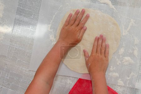 Photo for Close-up: children's hands rolling the dough into a layer. There is lot of flour on white table. - Royalty Free Image