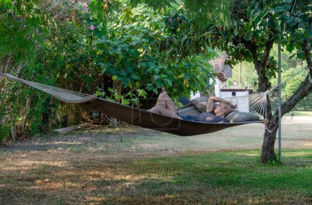 Photo for Woman relaxing in hammock in garden. White buildings in background. She is of European appearance - Royalty Free Image