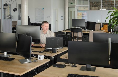 Foto de El hombre trabaja en la computadora en la oficina de TI. sala está llena de escritorios, sillas y monitores - Imagen libre de derechos