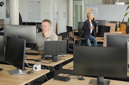 Téléchargez les photos : Deux hommes d'affaires travaillant ensemble dans un bureau informatique. La salle est pleine de bureaux, chaises et moniteurs. - en image libre de droit
