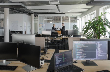 Foto de Dos empresarios que trabajan juntos en la oficina de TI. En primer plano están los monitores con código de programa en ellos. - Imagen libre de derechos
