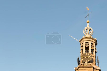 Munttoren Clock Tower, Amsterdam, vor blauem Himmel. Der Turm hat ein großes Zifferblatt und oben eine Wetterfahne. Hintergrund, Raum für Text, Kopierraum