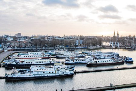 Photo for Oosterdok Canal and cruise ships moored for the night, Amsterdam. View from the top. The city in the background in the light of the setting sun. - Royalty Free Image