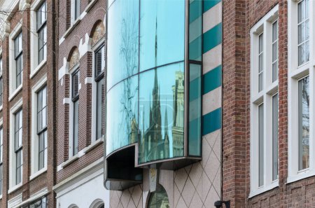 Modern large green glass window with reflection of the tower. Around the window in classical style. Amsterdam.