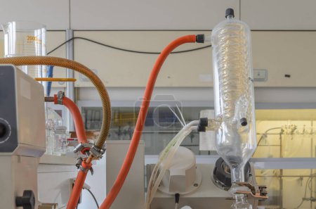 Glass discylator in a chemical laboratory. Apparatus with round bottom flask and cooling coil surrounded by other equipment. There is a window in the background.