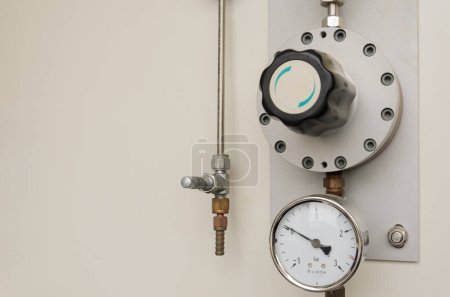 Description: A pressure gauge with a black dial and a red needle is mounted on a wall next to a valve. Copy space, background, place for text.