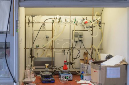 Aparato de laboratorio que contiene agitador magnético con una barra de agitación blanca y un vaso de vidrio colocado en la parte superior. Un frasco con líquido rojo, el otro con líquido transparente.