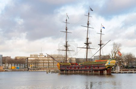 Photo for Large, three-masted replica ship docked in a harbor next to a historic building. Wooden frigate in Amsterdam. - Royalty Free Image