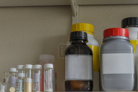 Photo for A shelf filled with various chemical bottles with labels. The labels contain information about the chemicals, including hazard symbols. - Royalty Free Image
