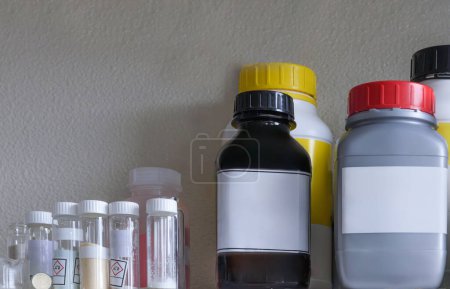 A shelf filled with various chemical bottles with labels. The labels contain information about the chemicals, including hazard symbols.