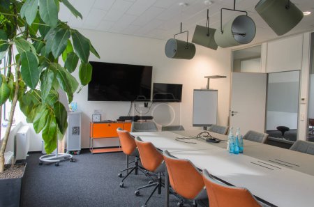 Bright conference room featuring a large table with comfortable chairs and a flat-screen television mounted on the wall. A potted plant adds a touch of life to the space. Lamps soffits on the ceilling