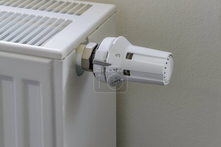 Photo rapprochée d'un simple radiateur blanc muni d'un thermostat tourné au maximum. Le radiateur est monté sur un mur blanc uni.