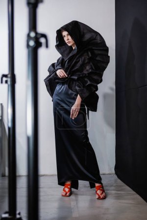 Foto de KYIV, UCRANIA - 01 DE FEBRERO DE 2019: Modelo lleva vestido negro con una capucha detrás del escenario FINCH show - Semana de la Moda Ucraniana Otoño Invierno 2019-2020 - Imagen libre de derechos