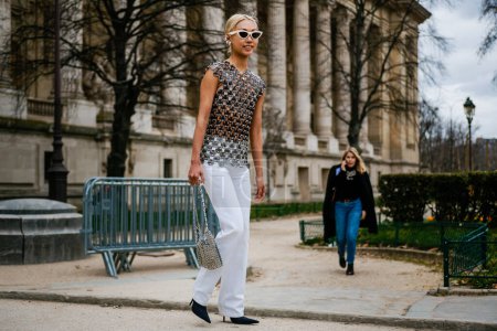 Téléchargez les photos : Un invité porte un haut Paco Rabanne en paillettes, un pantalon blanc, un sac en métal et des talons pointus noirs à l'extérieur du défilé PACO RABANNE, lors de la Fashion Week Femme Automne / Hiver 2019 / 2020 à Paris. - en image libre de droit