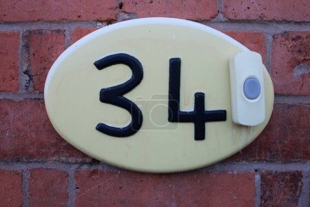 Foto de Base ovalada de plástico con números de puerta 34 Timbre inalámbrico adjunto, fondo de pared de ladrillo - Imagen libre de derechos