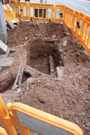 Road works, pavement dug up with exposed utility pipe and electrical cables and yellow plastic barrier, large hole in pavement