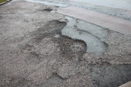 Photo for Crumbling deteriorated road surface taken after light rainfall - Royalty Free Image