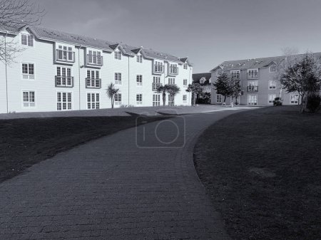 Téléchargez les photos : Photo monochrome des immeubles, du chemin et de l'herbe visible avec l'ombre du bâtiment - en image libre de droit