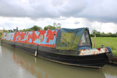 Grungy Narrow boat moored on riverbank, rust and green algae visble