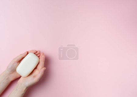 Photo for Woman's hands holding a soap on pastel pink background. Top view, flat lay. - Royalty Free Image