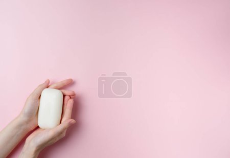 Photo for Woman's hands holding a soap on pastel pink background. Top view, flat lay. - Royalty Free Image