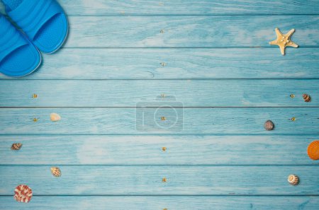 Flip-flops with shells on blue wooden background with copy space