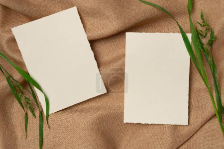 Two empty white sheets with grass on a fabric background from above. Copy space