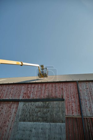 Reparatur eines Flachdachs eines landwirtschaftlichen Gebäudes mit einem gelben Mannlift an einem sonnigen Sommertag in Skaraborg Schweden
