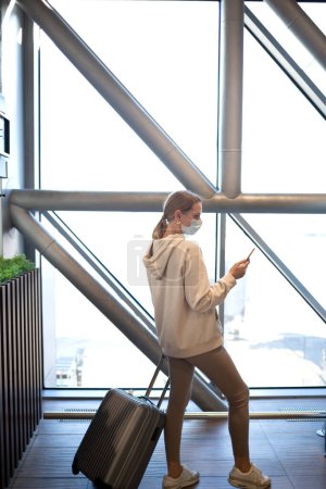 Photo for Young woman with suitcase waiting for check-in at the entrance to the airport. - Royalty Free Image