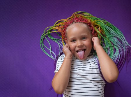portrait of a little beautiful girl with multi-colored pigtails, lying on a purple background.
